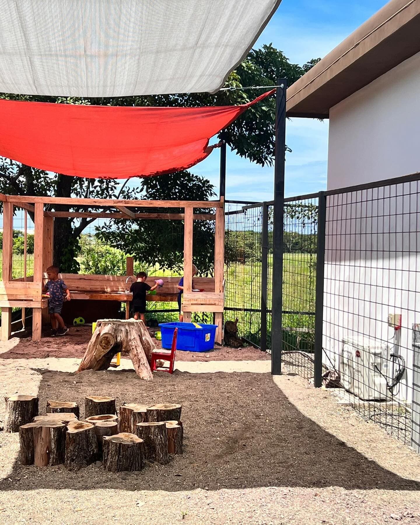 Journey students playing in the outdoor mud kitchen under the red shade sail at Tamarindo