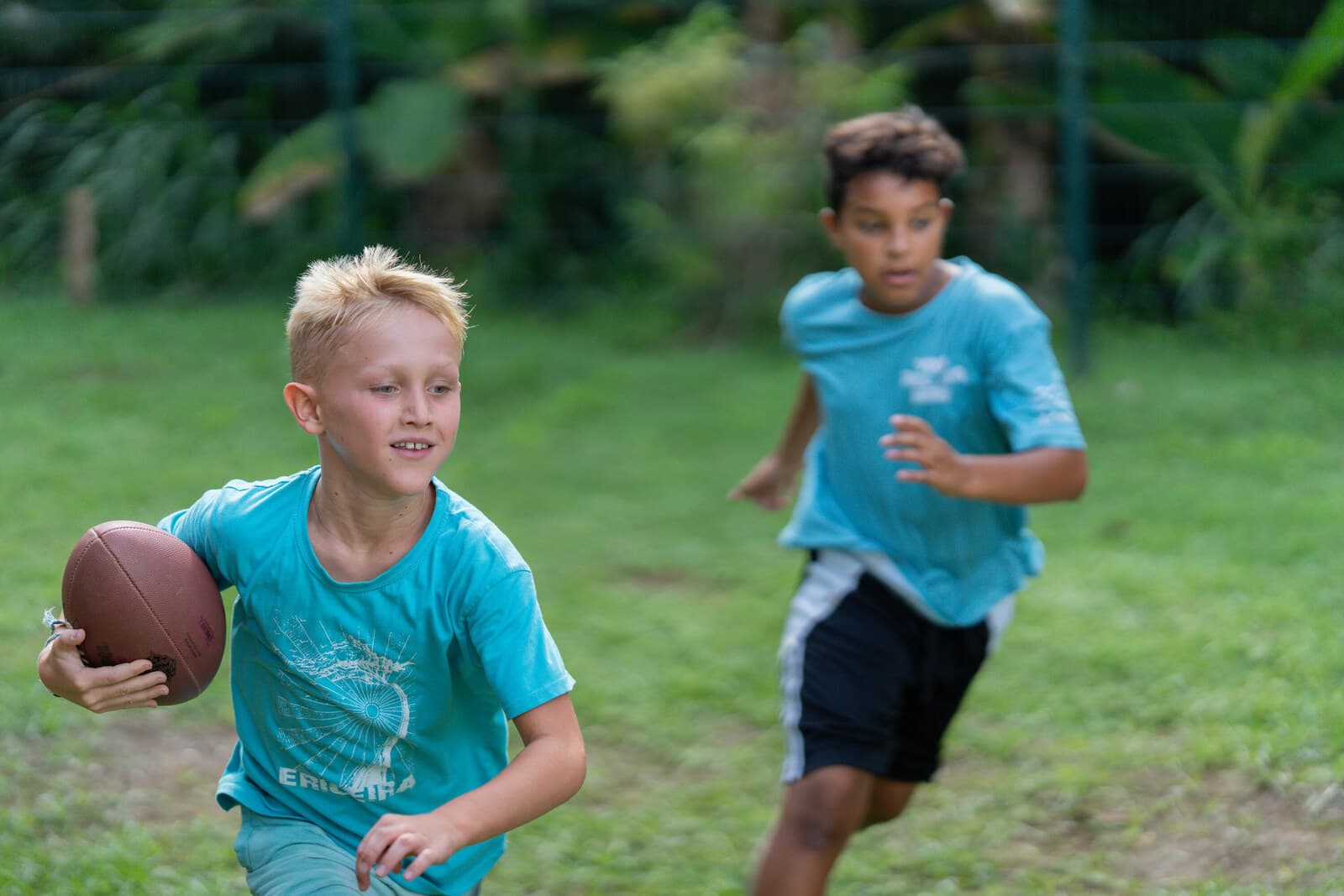 Two Journey students running with a football during a game on the Jacó grass field