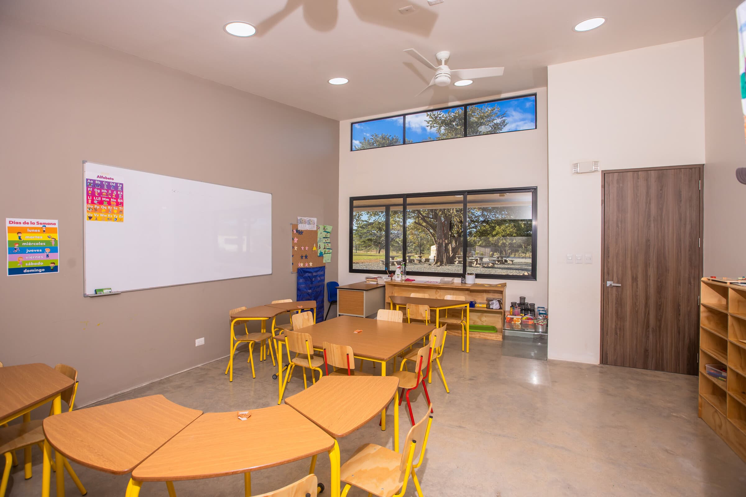 Bright Tamarindo primary classroom — yellow chairs, half-circle desks, big windows out to trees