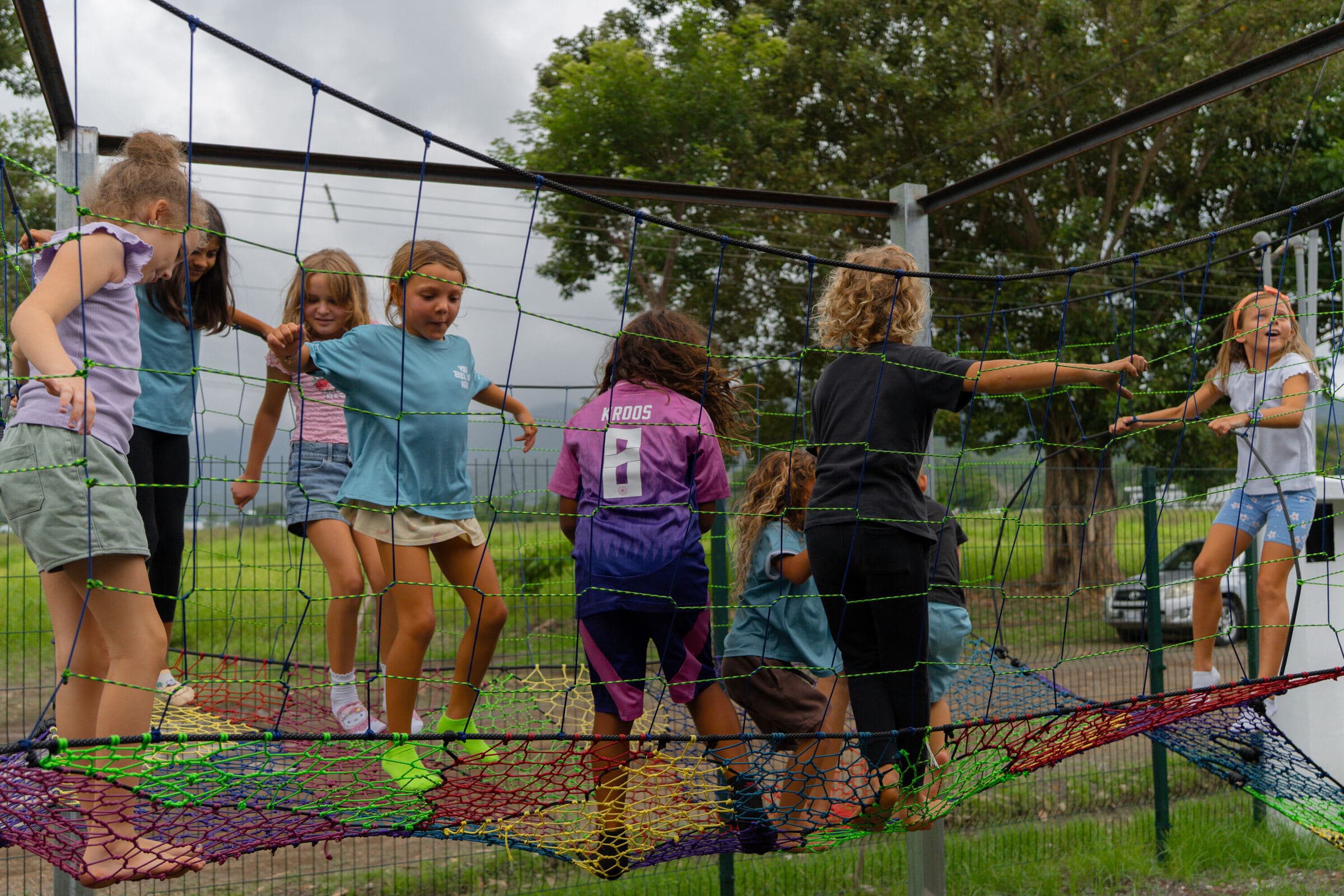 Kids climbing on the woven-rope outdoor play structure at the Jacó campus, rainforest mountains behind