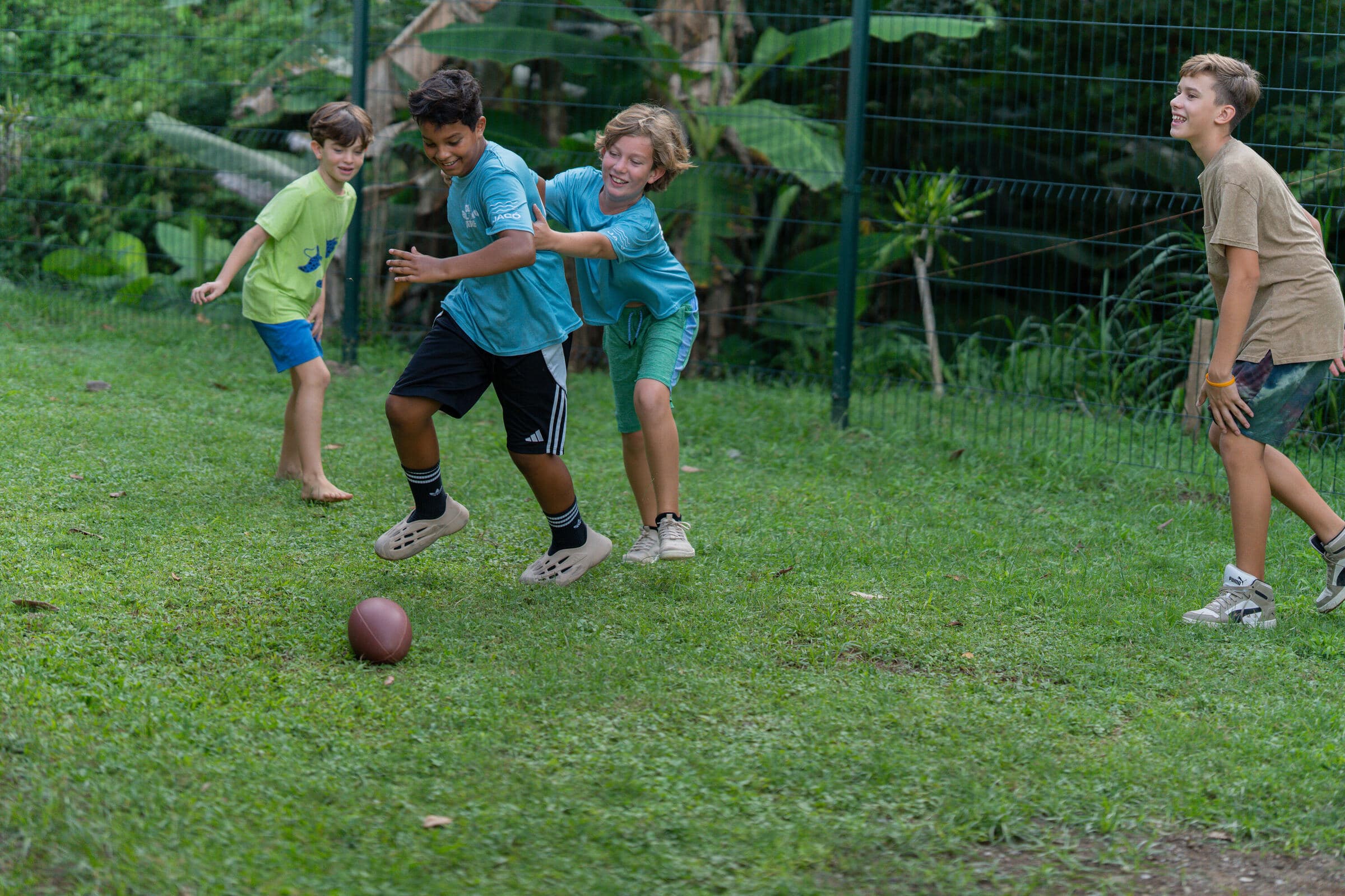 Journey students playing football on the Jacó grass field with rainforest fence behind
