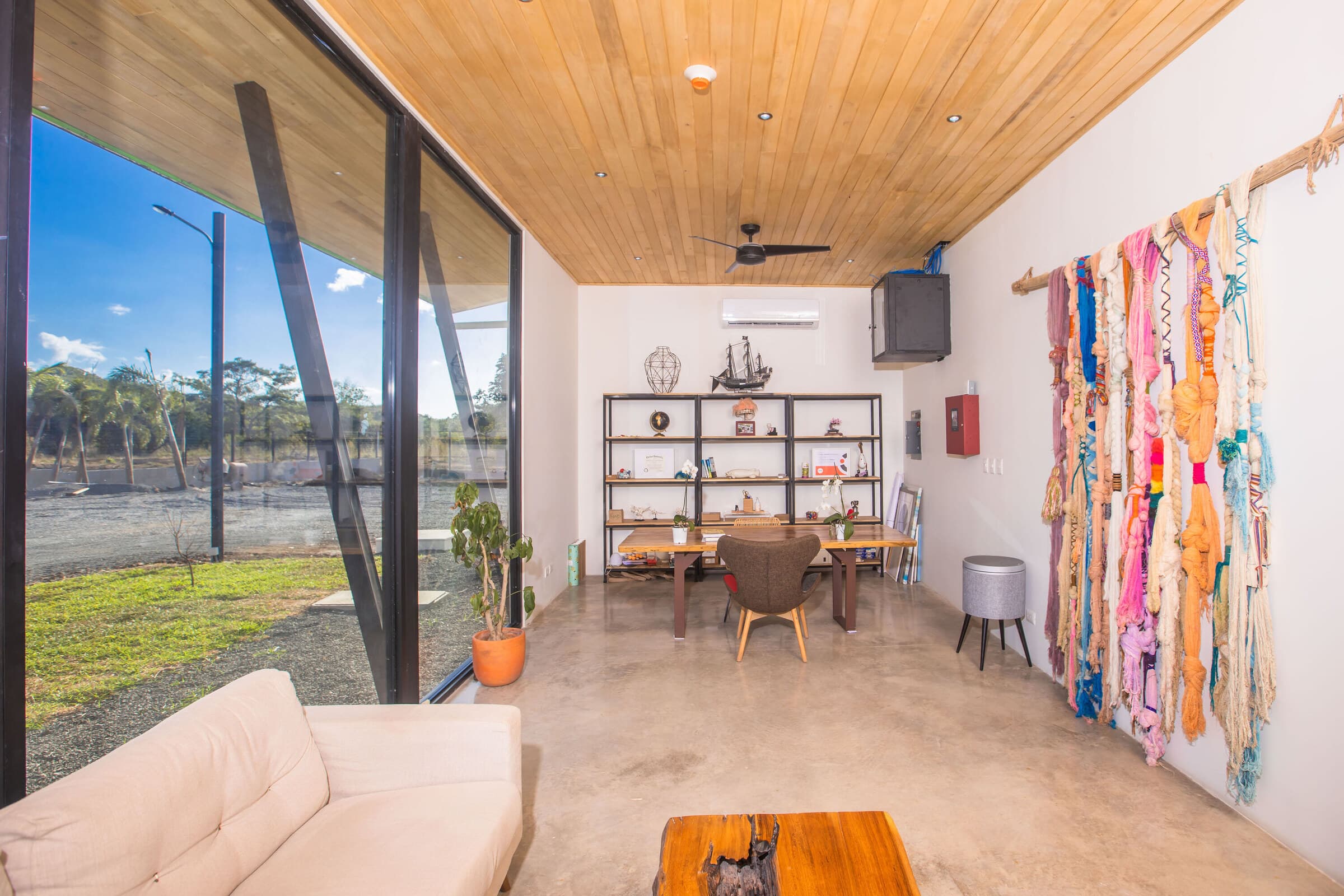 Tamarindo campus lounge interior — wood ceiling, glass walls onto landscape, large macrame wall hanging