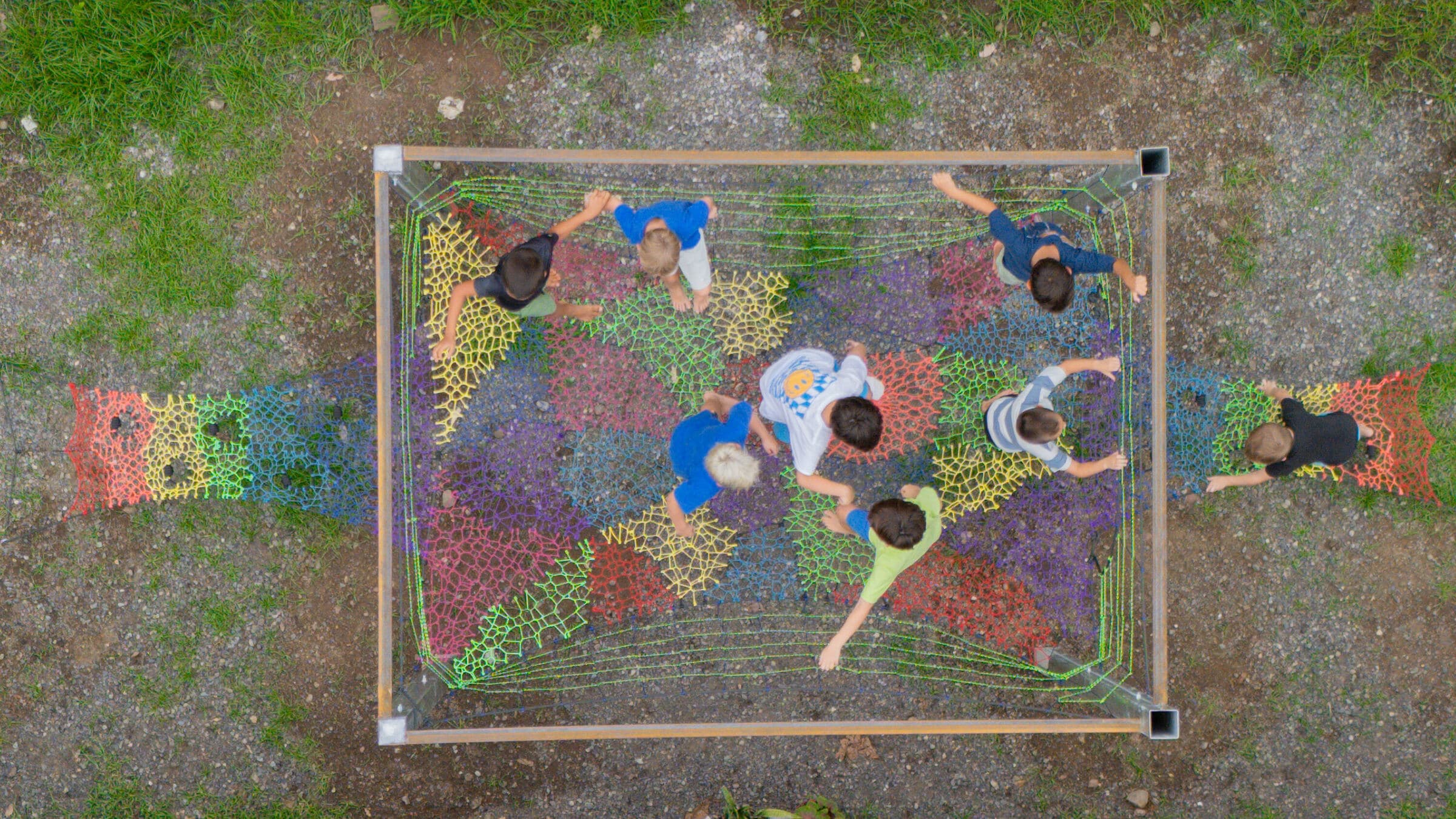 Overhead drone view of kids on the colorful rope-net play structure at the Jacó campus